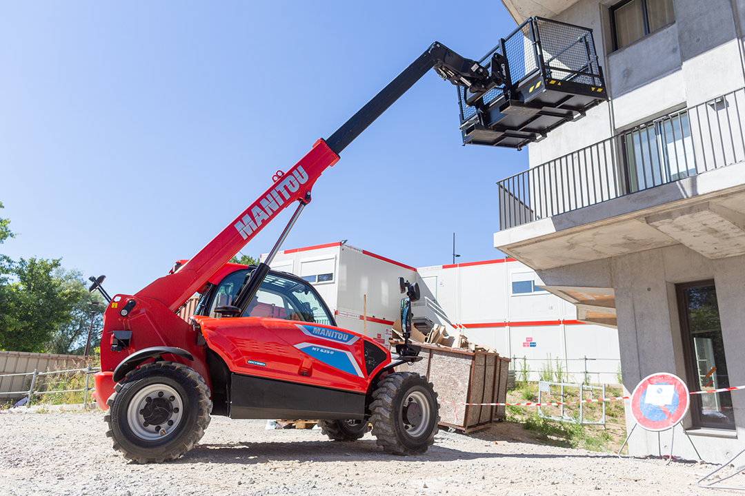 Manitou electric telehandler raising a man basket to a building